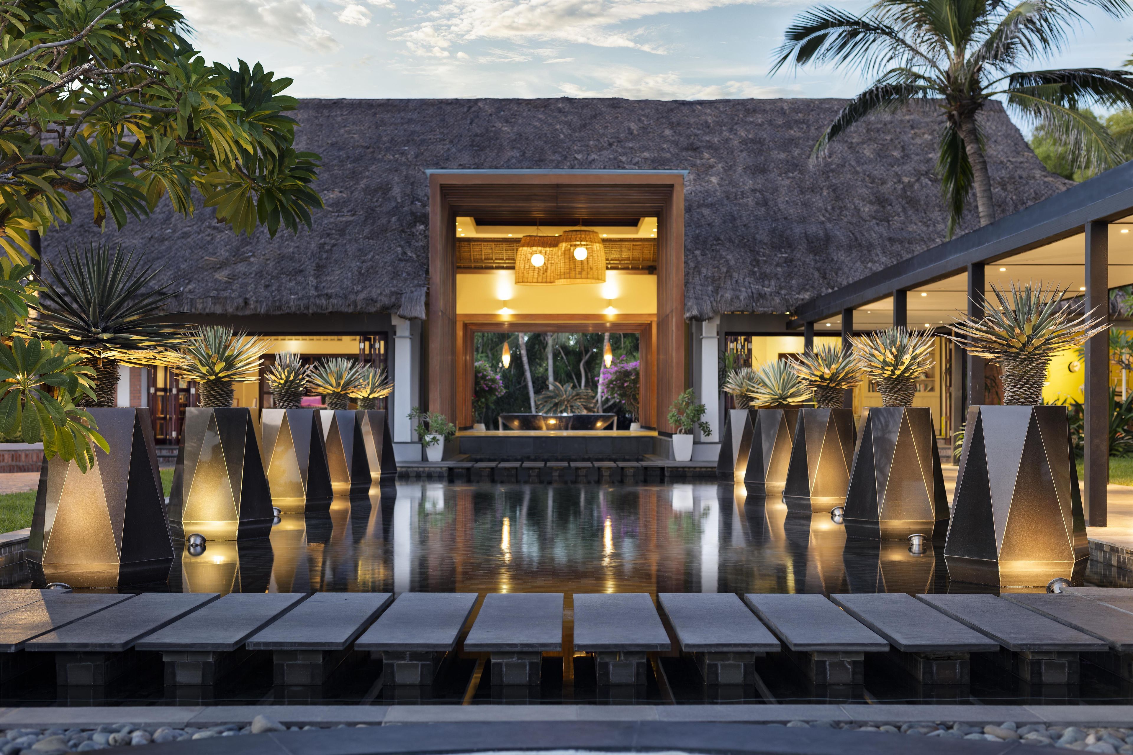 A modern resort with a pool, thatched-roof structure, and tropical plants.