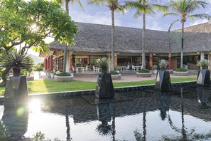 A resort with a pool, palm trees, and a thatched-roof building.