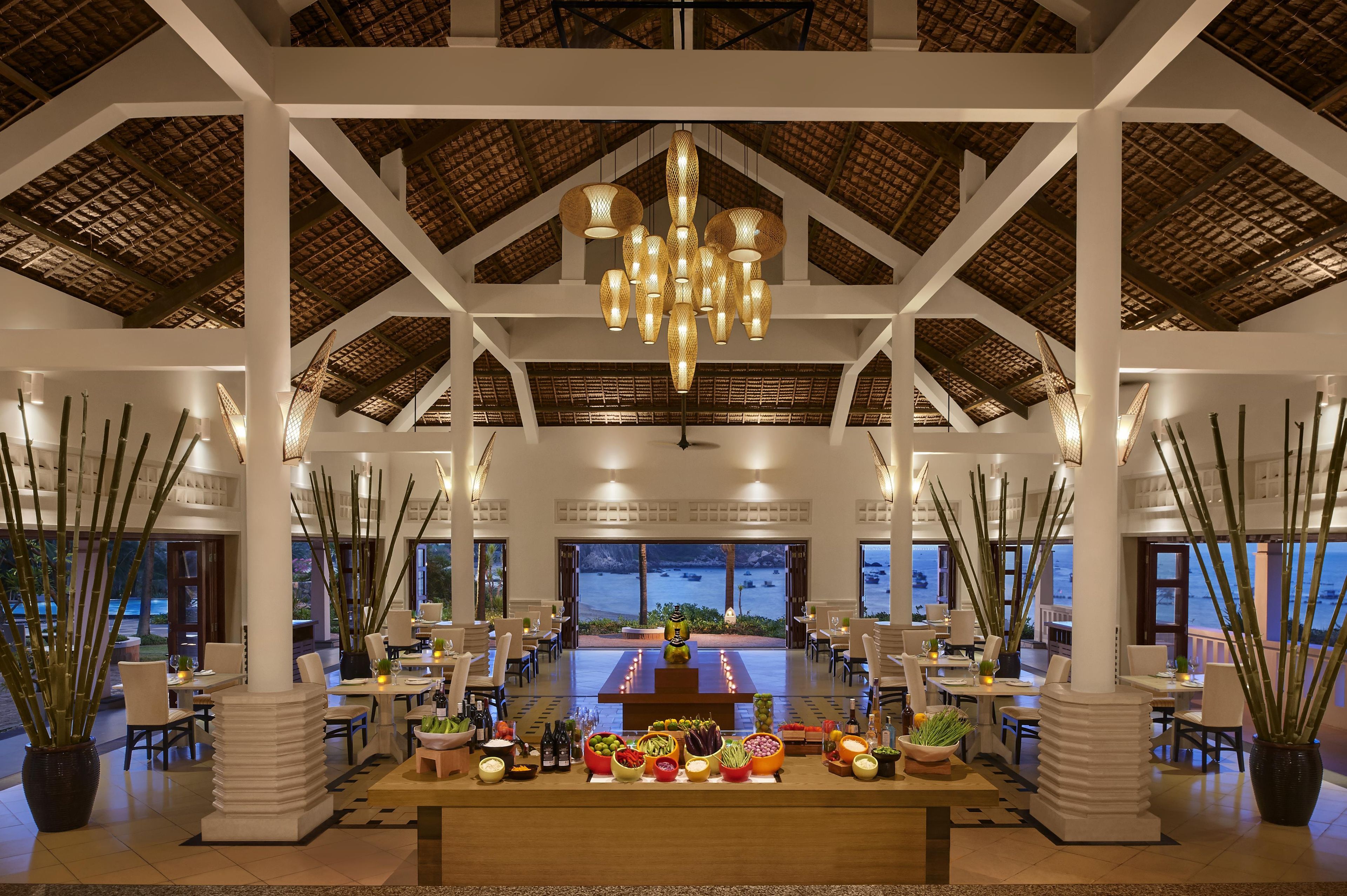 A spacious indoor dining area with high ceilings, a central chandelier, and a view of the sea.