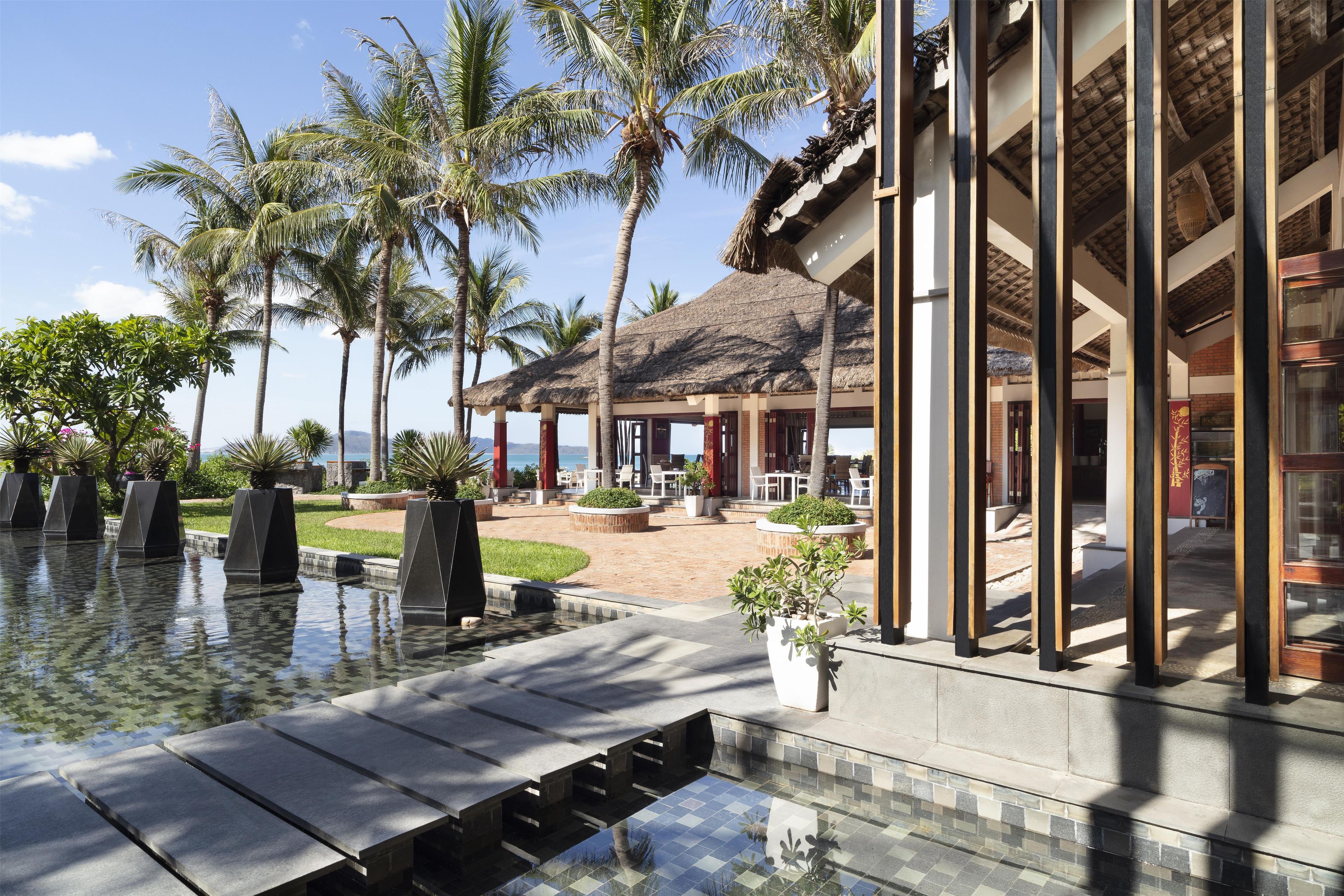 A resort with a pool, palm trees, and a covered outdoor seating area.