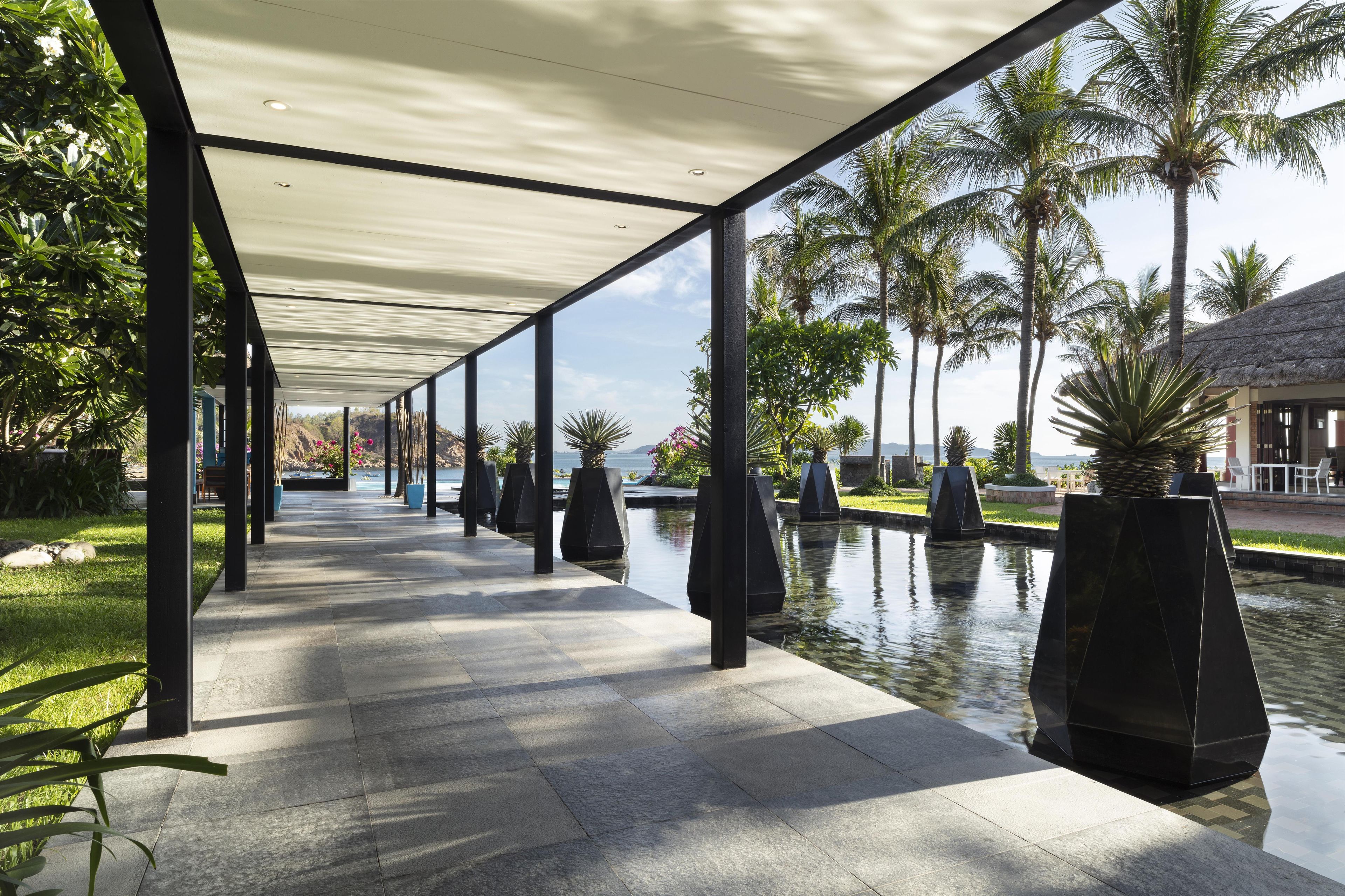 A covered walkway with a pool and palm trees.