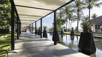 A covered walkway with a pool and palm trees.