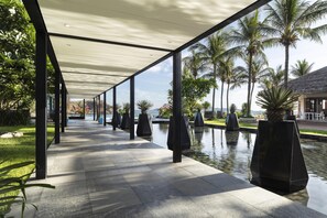 A covered walkway with a pool and palm trees. - Avani Quy Nhon Resort (Quy Nhon Nam)