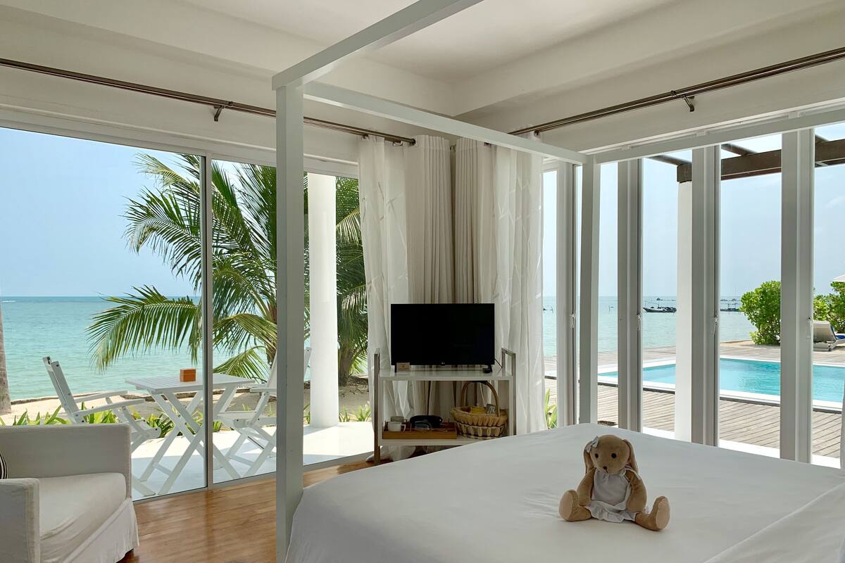 A bedroom with a large bed, a TV, and a view of the beach and ocean.