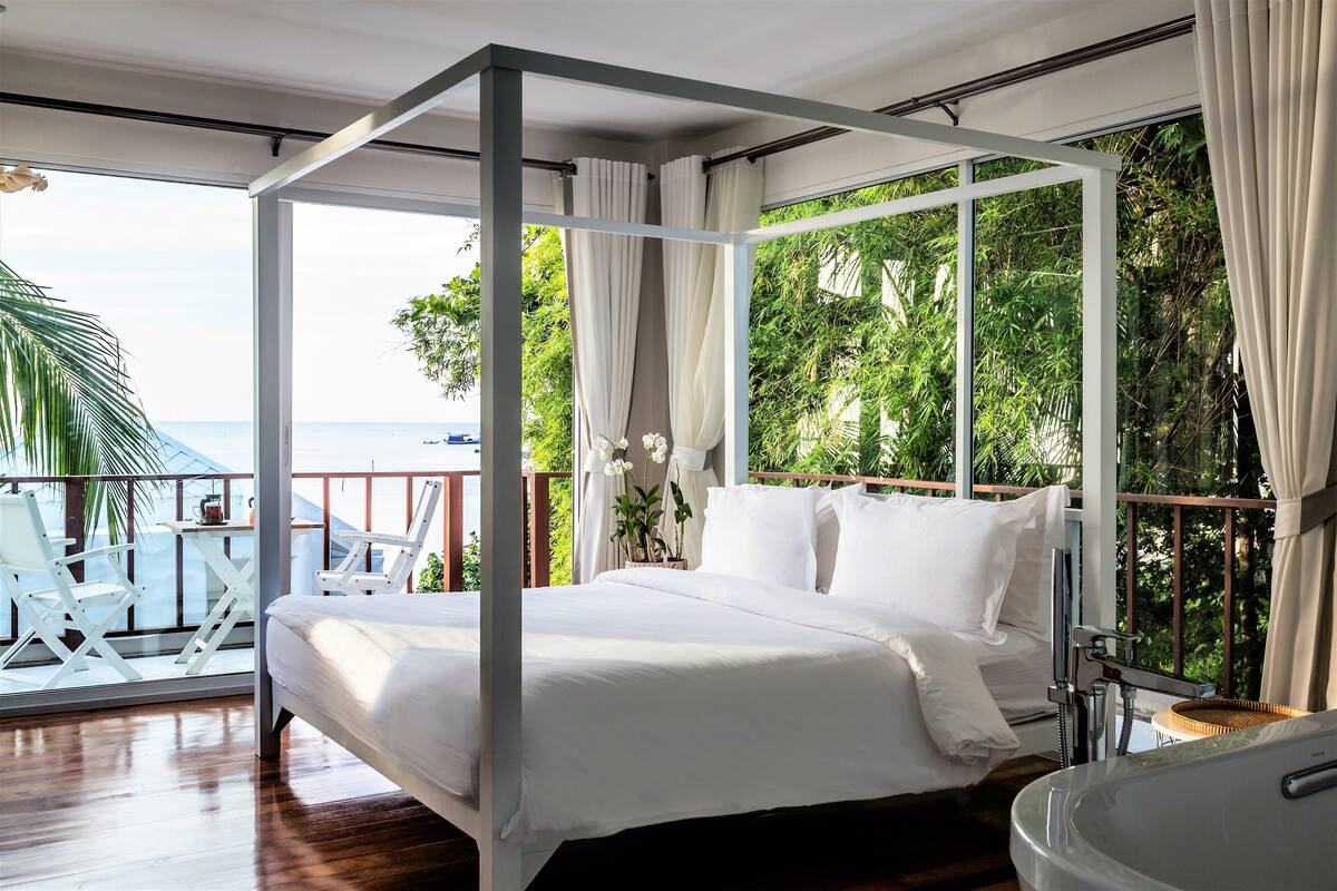 A spacious balcony with a bed, white curtains, and a view of the sea.