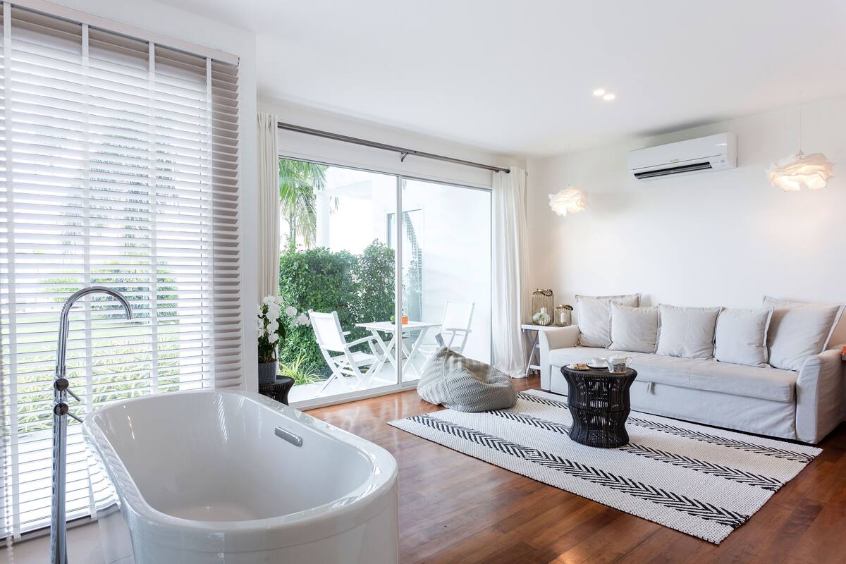 A modern living room with a white bathtub, a white sofa, and a dining area with white chairs.