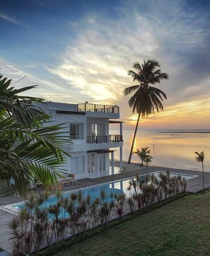 A modern two-story house with a pool, surrounded by palm trees and a view of the ocean at sunset. - Villa Nalinnadda Petite Hotel & Spa - Adults Only (Koh Samui)
