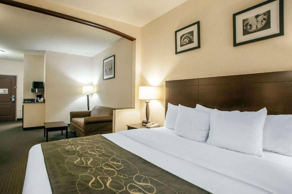 A hotel room with a bed, a desk, a chair, and a kitchenette.