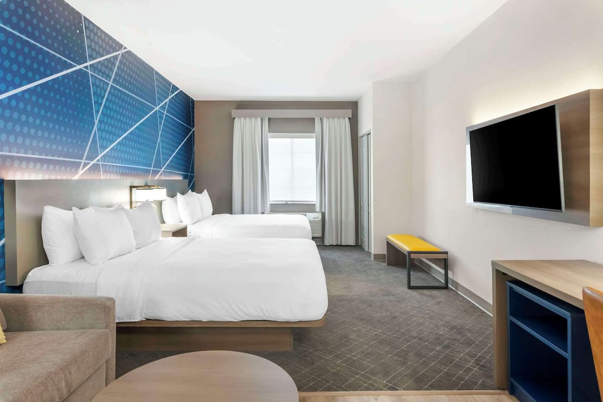 A hotel room with a large bed, a TV mounted on the wall, a small table, and a bench.
