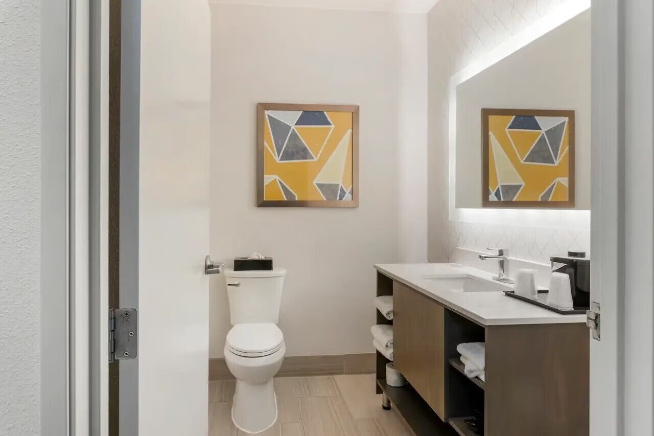 A modern bathroom with a toilet, sink, and mirror. There are two framed artworks on the wall.