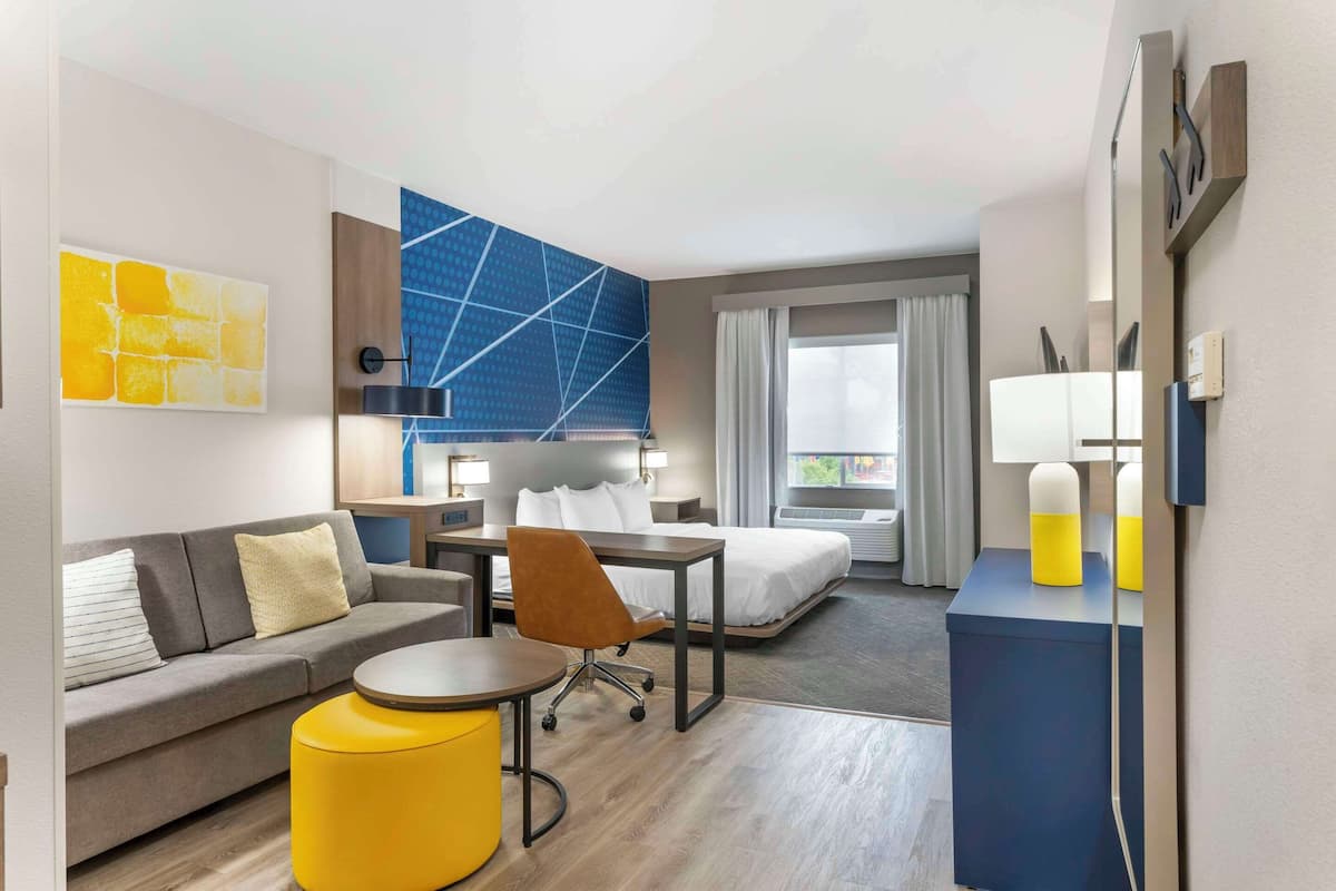 A modern hotel room with a sofa, a small round table, a bed, and a desk.