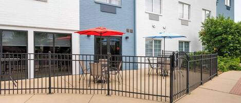 A building with a blue and white facade, outdoor seating with red and blue umbrellas, and a gated entrance.