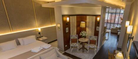 A hotel room with a large bed, a sofa, a small table with chairs, and a desk with a lamp.
