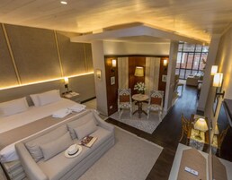 A hotel room with a large bed, a sofa, a small table with chairs, and a desk with a lamp.