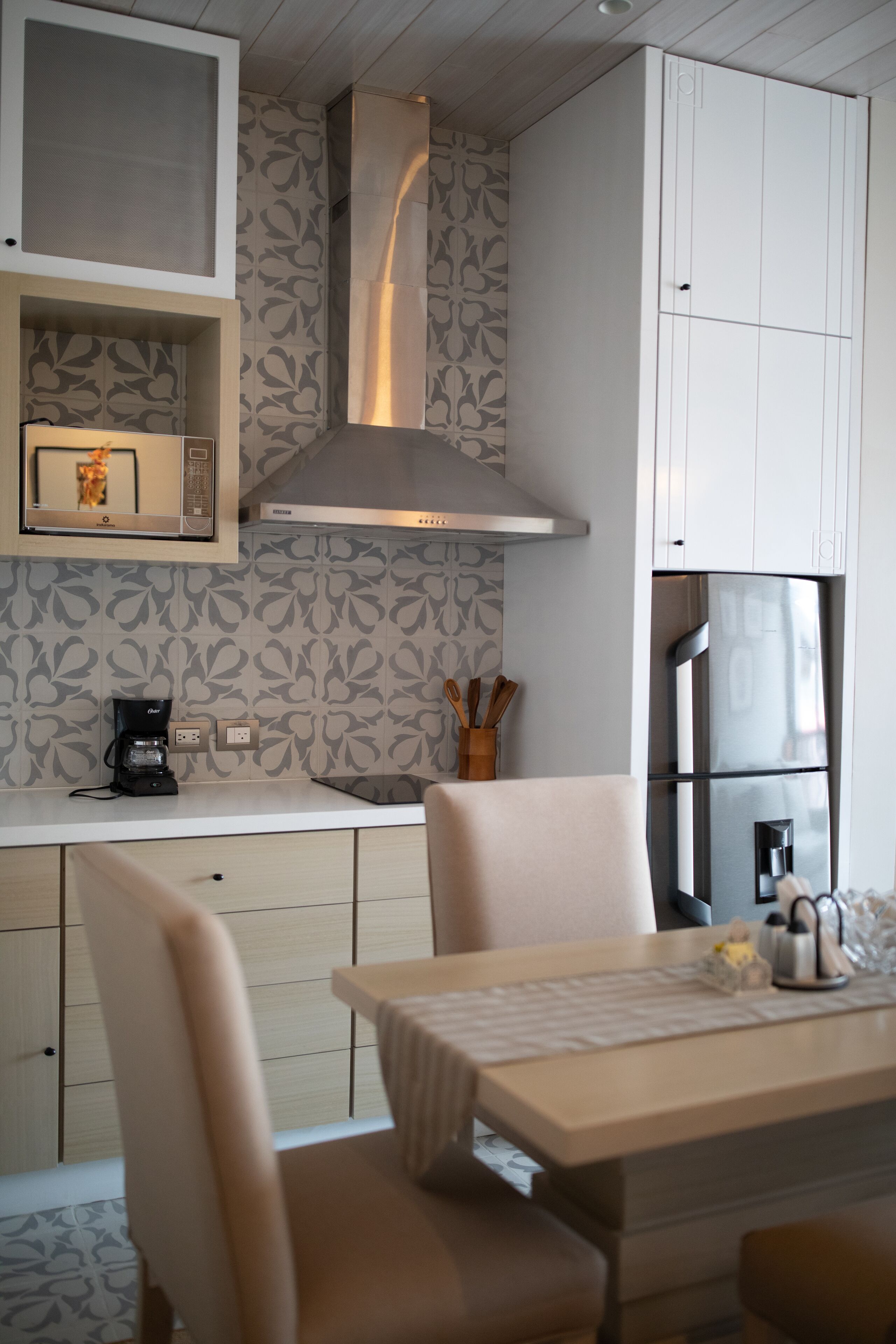 Una cocina moderna con microondas integrado, refrigerador de acero inoxidable y estufa a gas. Hay una mesa de comedor con sillas y una cafetera en la encimera.