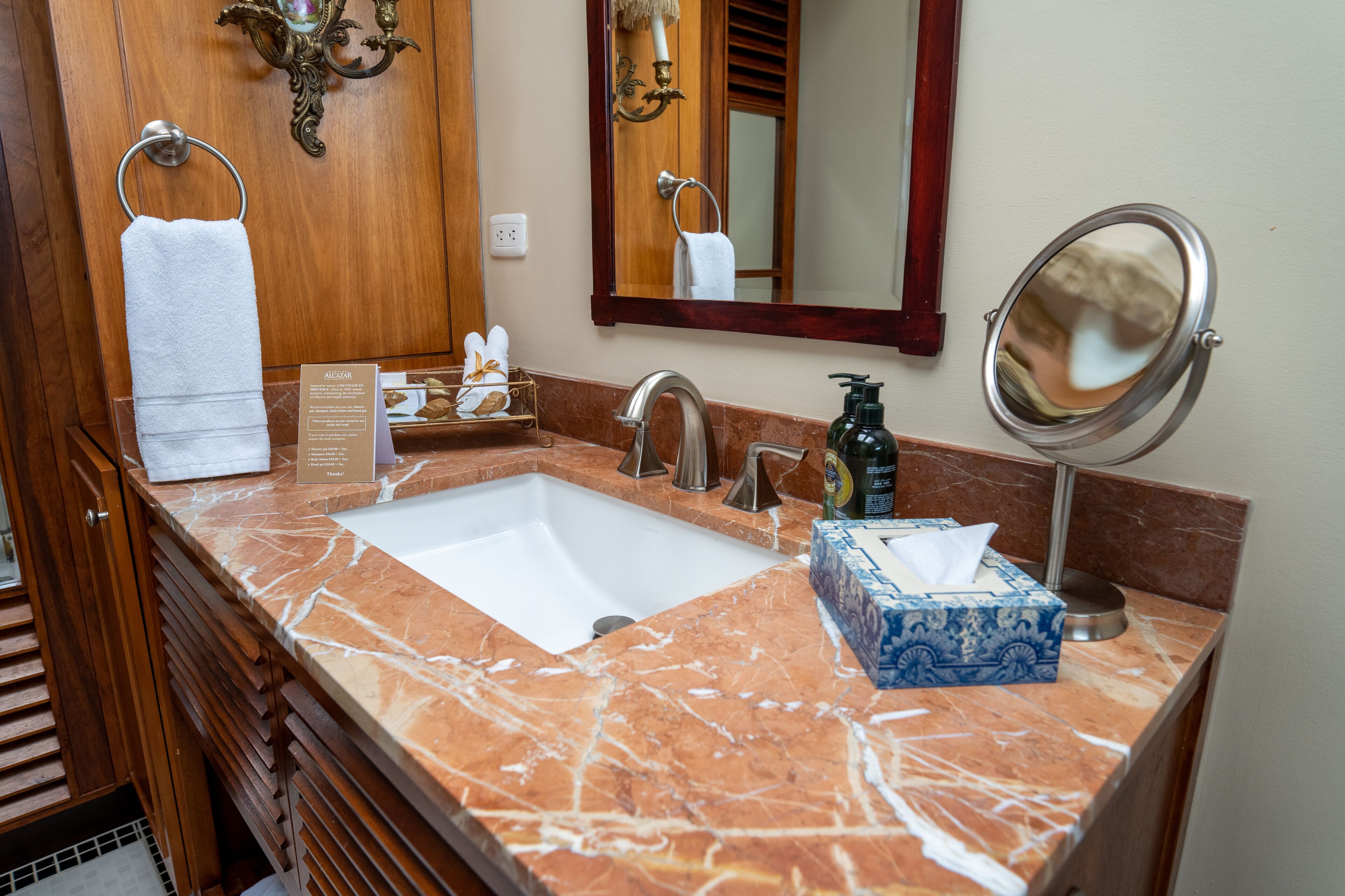 A bathroom with a marble sink, a mirror, a towel rack, and a box of tissues.