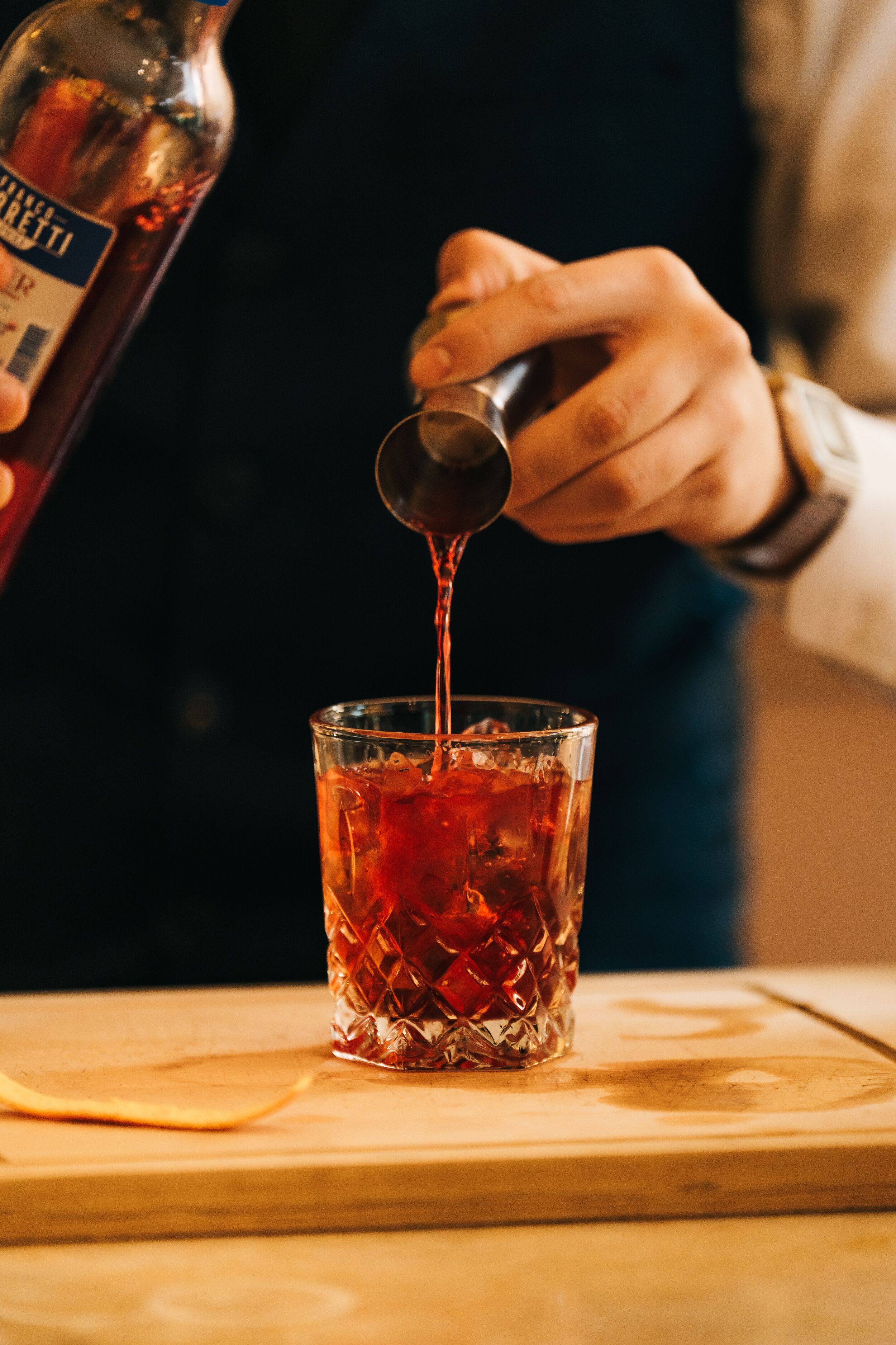 A person pouring a dark liquid from a bottle into a glass with ice cubes.