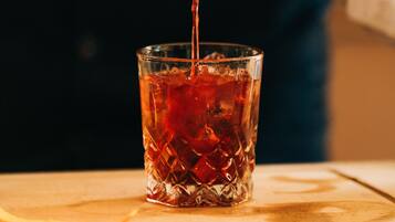 A person pouring a dark liquid from a bottle into a glass with ice cubes.