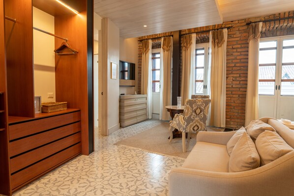 Habitación de hotel con un armario de madera, un sofá, una pequeña mesa, un televisor y una ventana con cortinas.