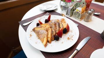 A breakfast plate with pancakes, strawberries, and blackberries, a knife, and a spoon on a table with a placemat.