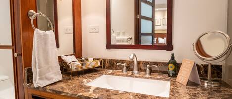 Un baño con encimera de mármol, un lavabo, un espejo, un perchero para toallas y una botella de champú.