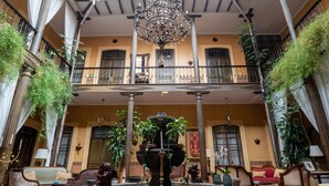 Un amplio atrio con una fuente central, candelabros ornamentales y abundante vegetación.