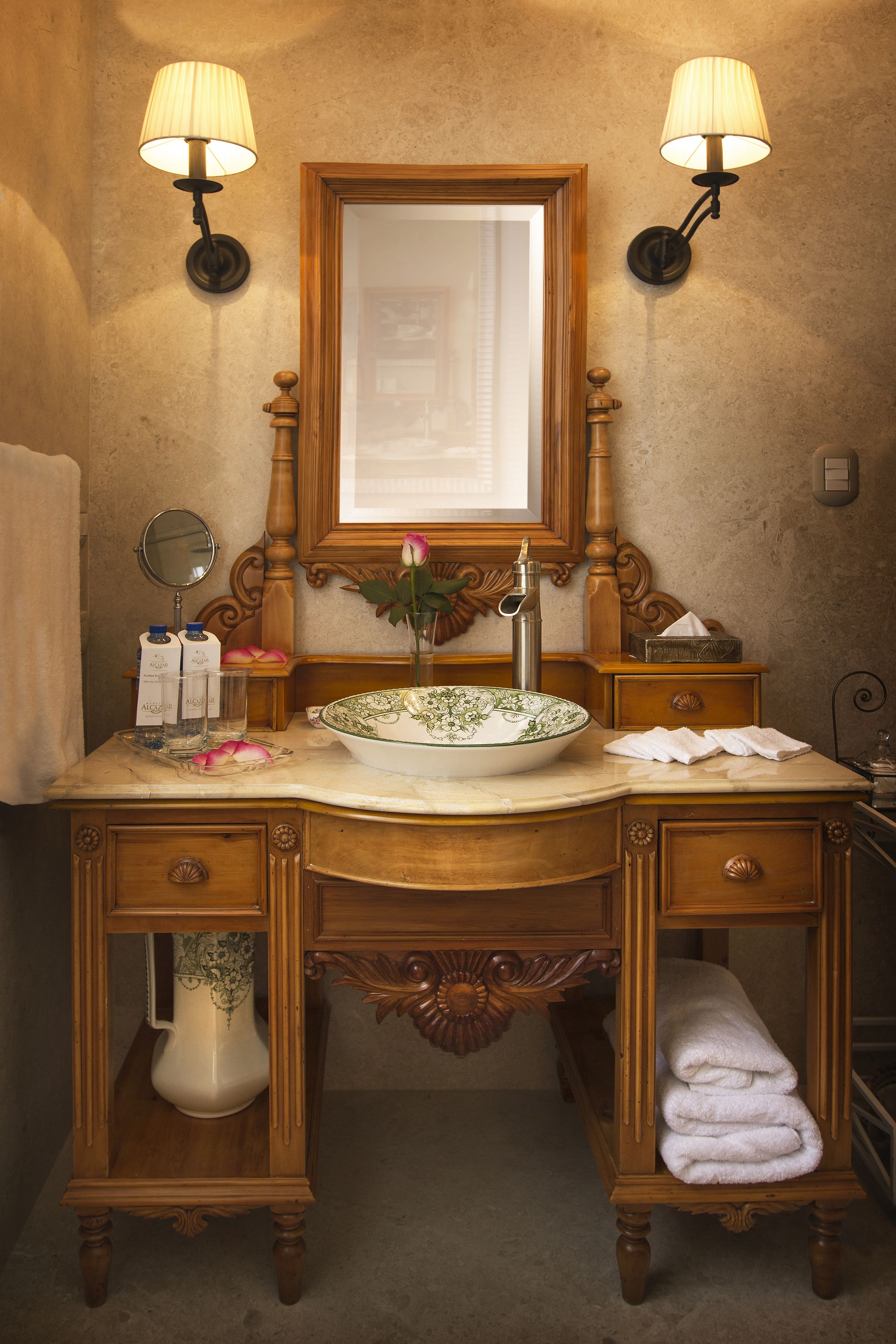 Un mobile bagno in legno con uno specchio grande, due luci a parete, un lavabo e un vaso con un fiore.