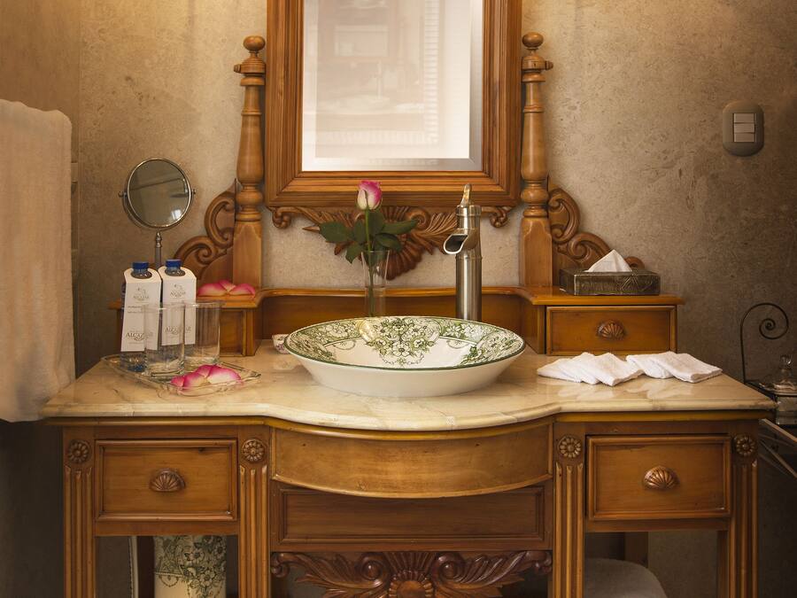 A wooden vanity with a large mirror, two wall sconces, a bowl sink, and a vase with a flower.