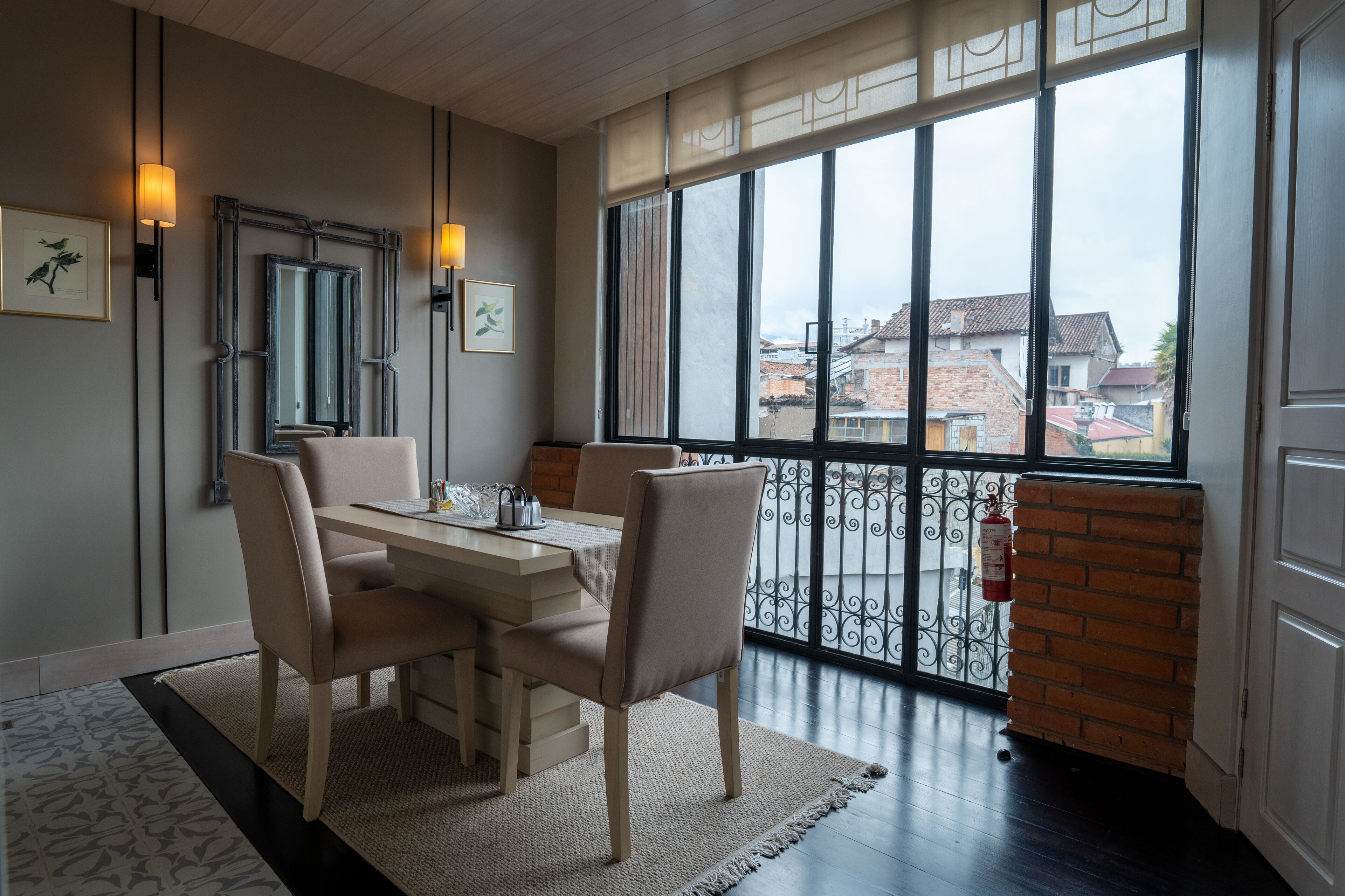 A dining area with a table and chairs, a large window with a view of buildings, and a fire extinguisher near the window.