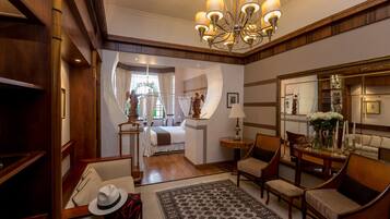A hotel room with a large mirror, a chandelier, a bed with curtains, a sitting area with chairs, and a rug.