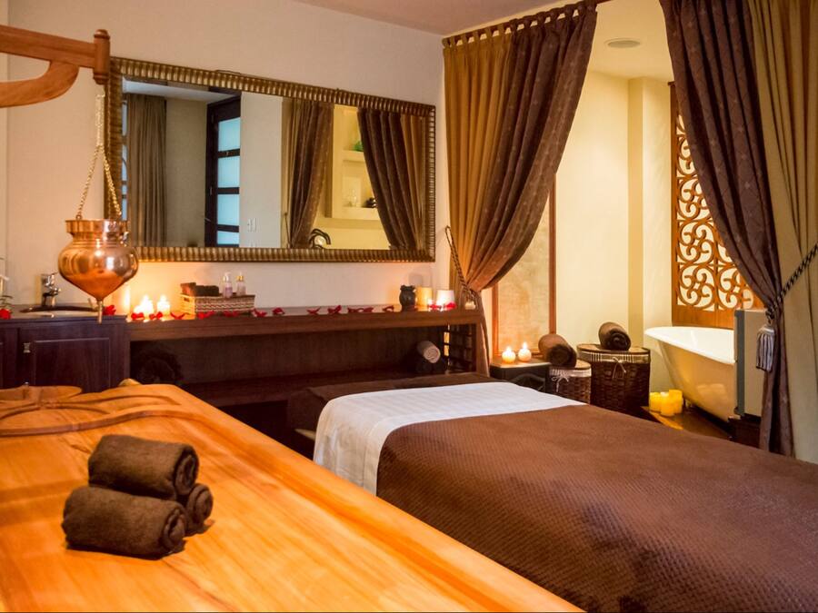 A hotel room with a large bed, a wooden headboard, a mirror, a vanity with a sink, and a decorative curtain.