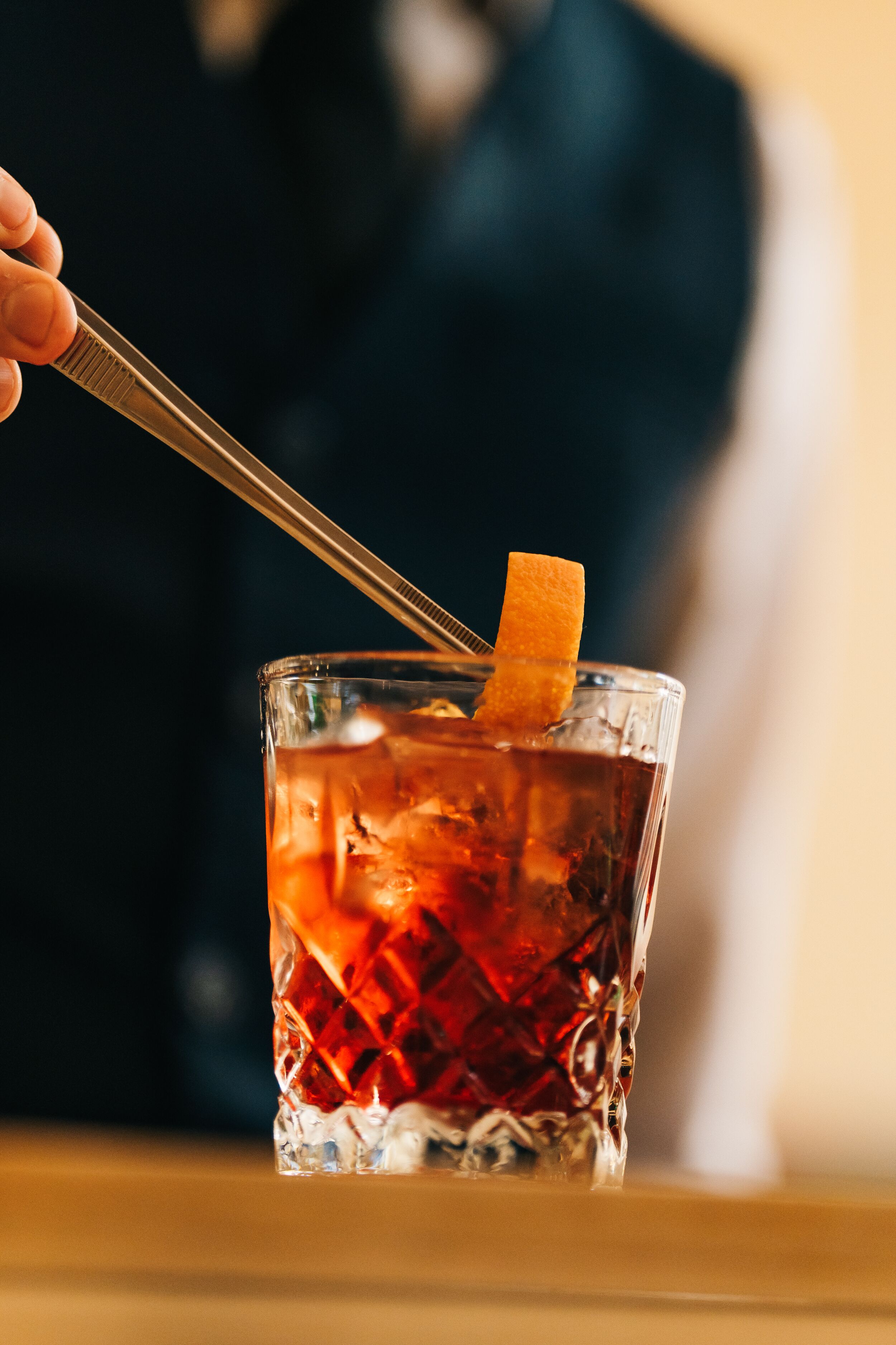 A close-up of a cocktail with an orange peel garnish, served in a textured glass.