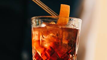 A close-up of a cocktail with an orange peel garnish, served in a textured glass.