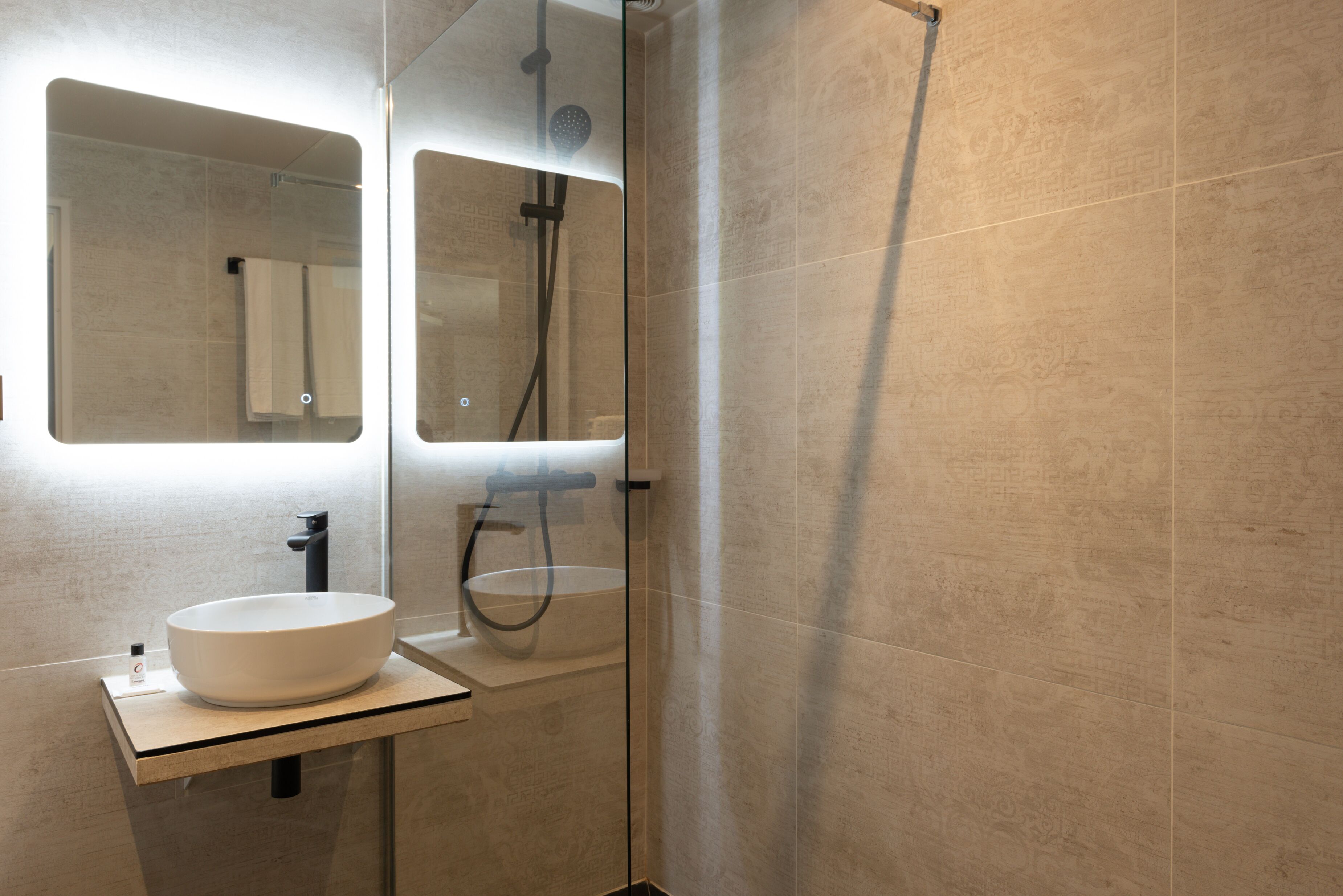 A modern bathroom with a large mirror, a white sink, and a glass-enclosed shower area.