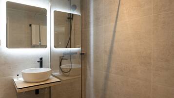 A modern bathroom with a large mirror, a white sink, and a glass-enclosed shower area.