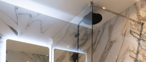 Une salle de bain moderne avec un meuble-lavabo en marbre, une douche à parois de verre et un grand miroir doté d’un éclairage intégré.
