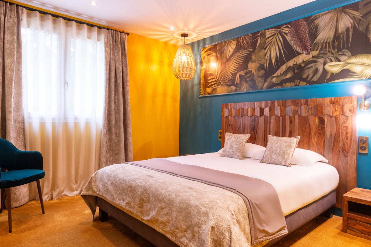 Quarto com uma cama grande, uma cadeira, uma cabeceira de madeira, um quadro e um candeeiro suspenso.