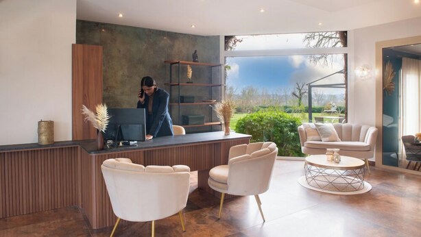 A modern reception area with a wooden desk, two white armchairs, and a round coffee table. - The Originals Boutique, Parc Hôtel, Orléans Sud (La Chapelle-Saint-Mesmin)