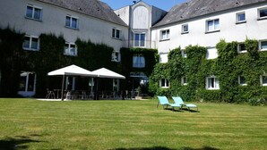 A courtyard with a lawn, outdoor seating, and a building with multiple windows and a central entrance. - The Originals Boutique, Parc Hôtel, Orléans Sud (La Chapelle-Saint-Mesmin)