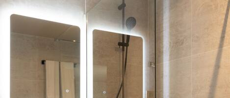 Un baño moderno con ducha de vidrio, un lavamanos blanco y un espejo encima.
