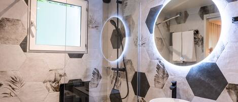 A modern bathroom with a glass-enclosed shower, a large mirror with a circular frame, and a white sink.