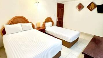 A hotel room with two single beds, a wooden headboard, a nightstand, and a small table.