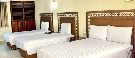 A hotel room with three single beds, wooden headboards, and a tiled floor.