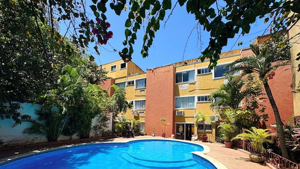 A swimming pool surrounded by lush greenery and a multi-story building with balconies. - Suites Cancun Center Cancun (Cancun)