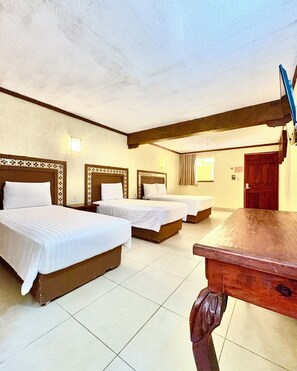 Habitación de hotel con tres camas, una mesa de madera y un techo con vigas a la vista.