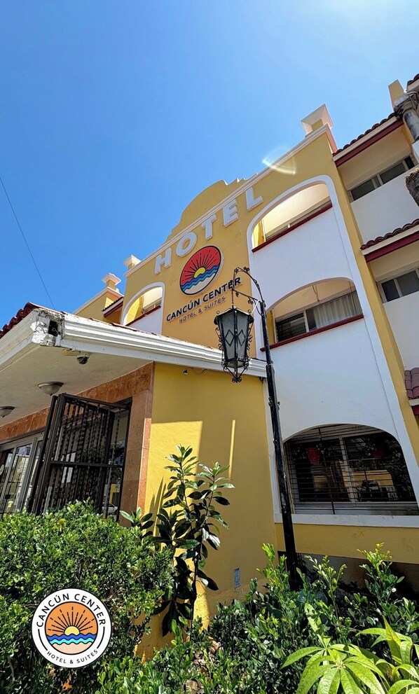 Un hotel con fachada amarilla, un letrero que dice "HOTEL" y el logo de Cancun Center Hotel & Suites.