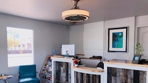 Un mostrador de recepción con detalles de madera, una silla azul y una obra de arte enmarcada en la pared.