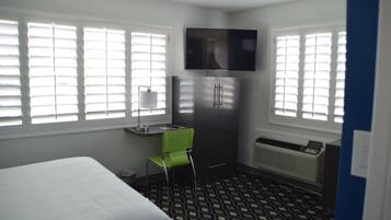Una habitación de hotel con cama, escritorio con silla, televisor montado en la pared y refrigerador.