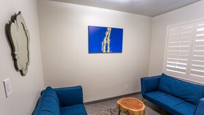 Una sala de estar con dos sofás azules, una mesa de centro de madera, un cuadro azul y un espejo en la pared.