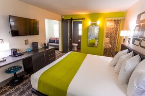 A hotel room with a bed, a desk with a coffee maker, a TV, and a bathroom with a shower curtain.